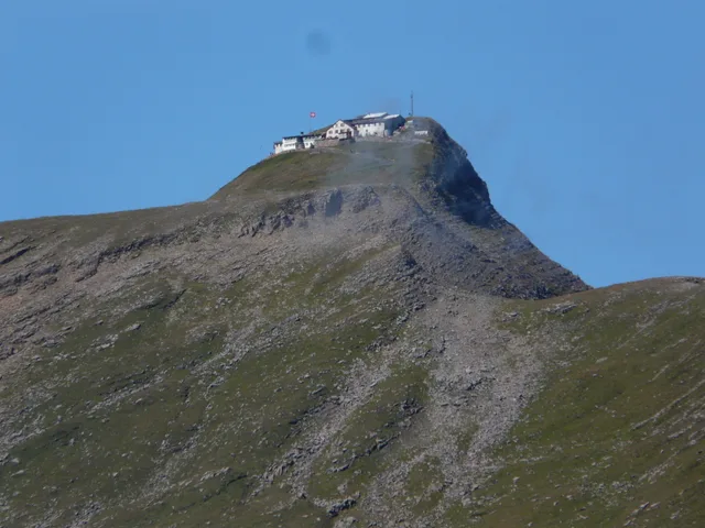 Der Gipfel des Faulhorns mit dem Berghotel auf dem Grat, darunter Schutthänge und Grasflanken vor wolkenlosem Himmel