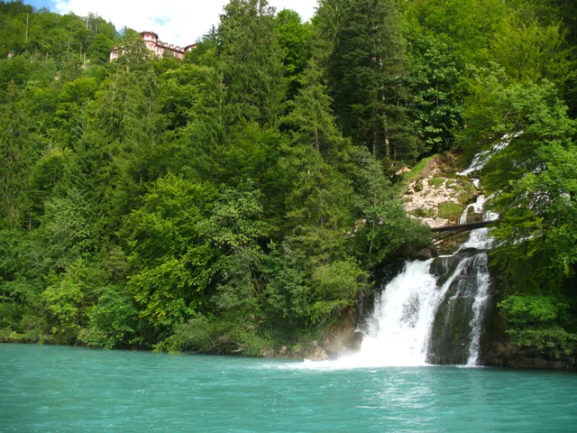 One tier of the Giessbach Falls dropping into turquoise water between dense forest, the Grandhotel Giessbach visible among the trees above