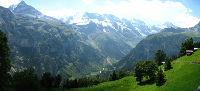Blick von Gimmelwald über steile Wiesen ins Lauterbrunnental auf die verschneiten Gipfel gegenüber