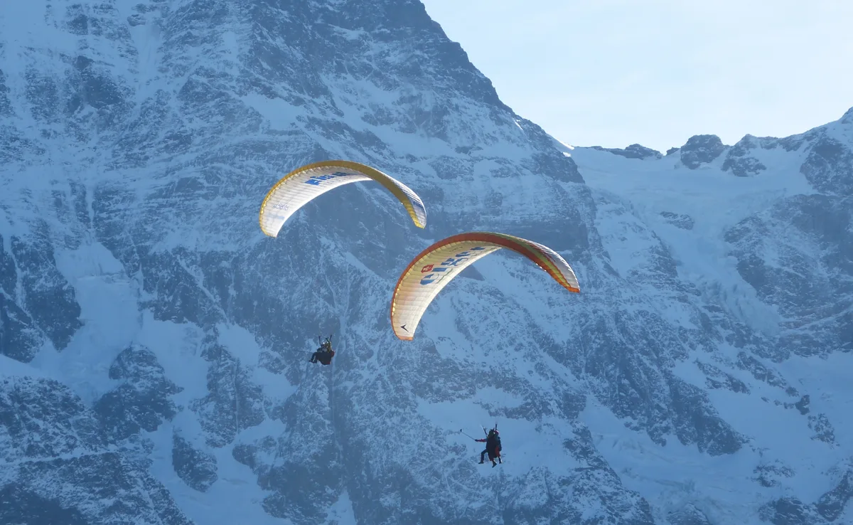 Zwei Gleitschirme im Flug vor einer verschneiten Felswand oberhalb von Mürren