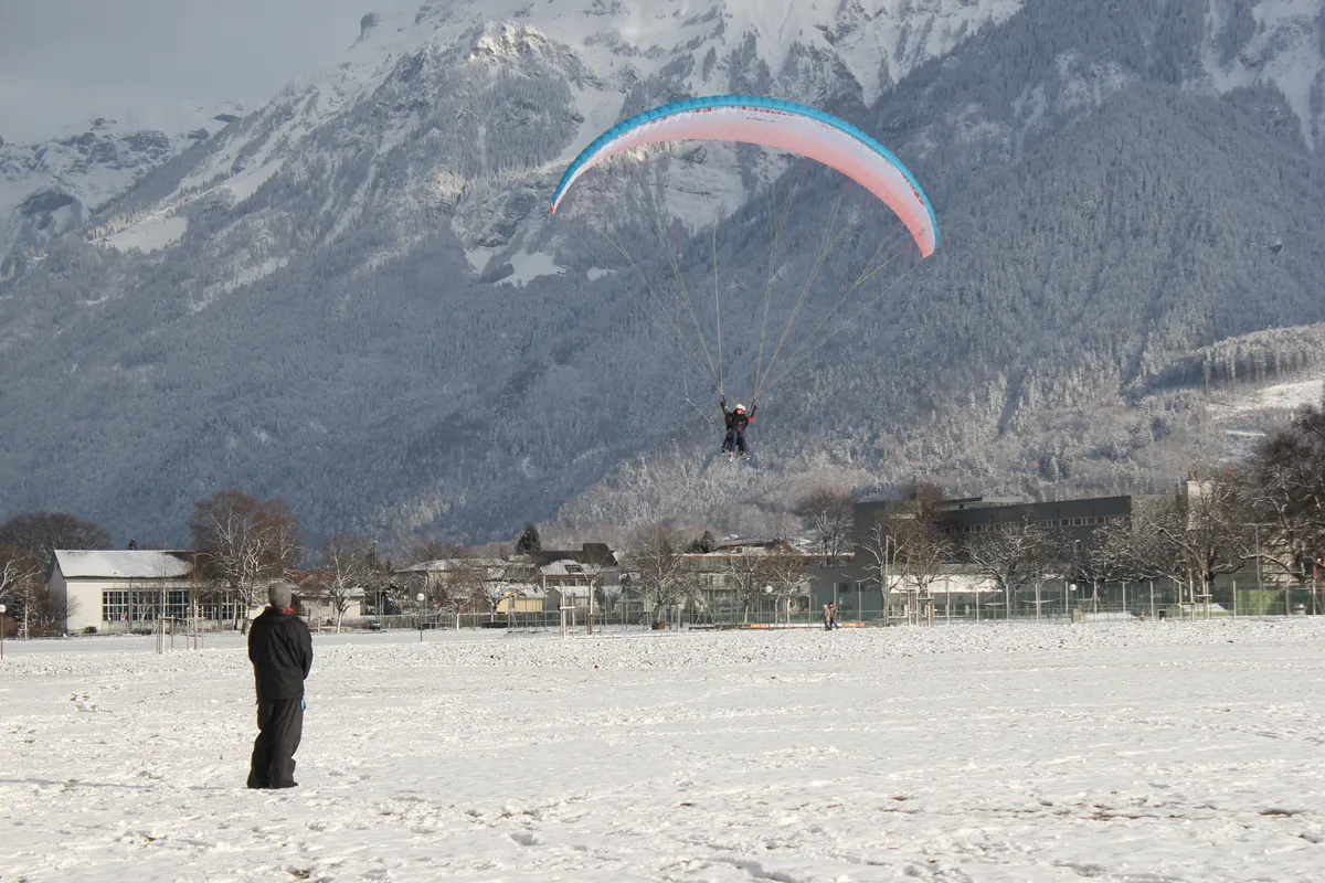 Gleitschirm kurz vor der Landung auf der verschneiten Höhematte in Interlaken, eine wartende Person im Vordergrund
