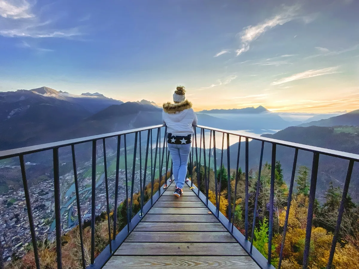 Eine Person steht auf dem Zwei-Seen-Steg des Harder Kulm und blickt in der Abendsonne über Interlaken und das Tal