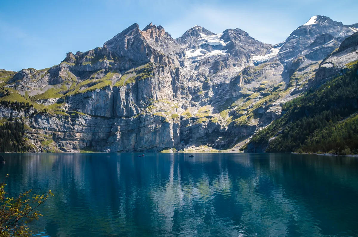 Der Oeschinensee vor der Felswand der Blüemlisalp, deren Schneefelder sich im tiefblauen Wasser spiegeln