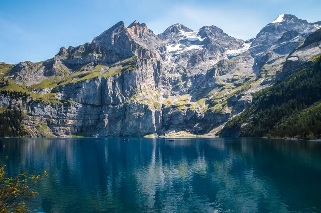 Der Oeschinensee vor der Felswand der Blüemlisalp, deren Schneefelder sich im tiefblauen Wasser spiegeln