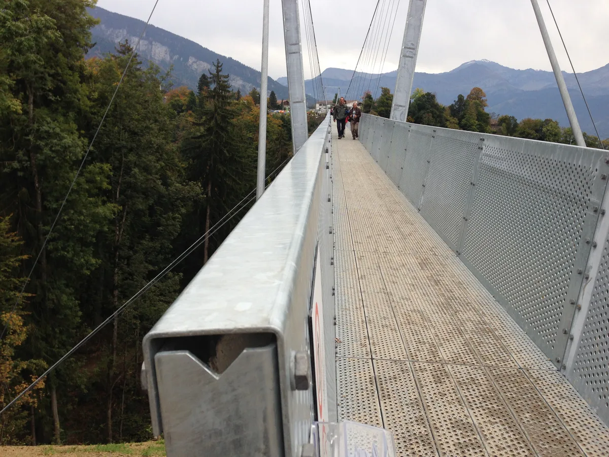 Der Steg der Panoramabrücke Sigriswil mit Gitterrost und Geländer, weiter hinten Personen auf der Brücke vor den Bergen