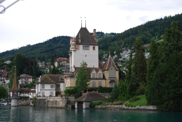 Schloss Oberhofen mit seinem Turm direkt am Ufer des Thunersees, dahinter der bewaldete Hang