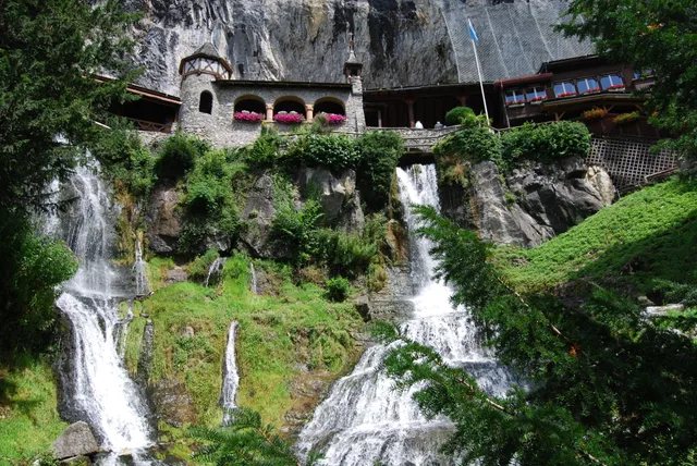 The entrance building of the St Beatus Caves, with its arcaded gallery set into the cliff face and two waterfall strands cascading down the green slope below