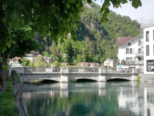 Die steinerne Bogenbrücke über die grüne Aare in Unterseen, dahinter Altstadthäuser und bewaldete Felsflanke